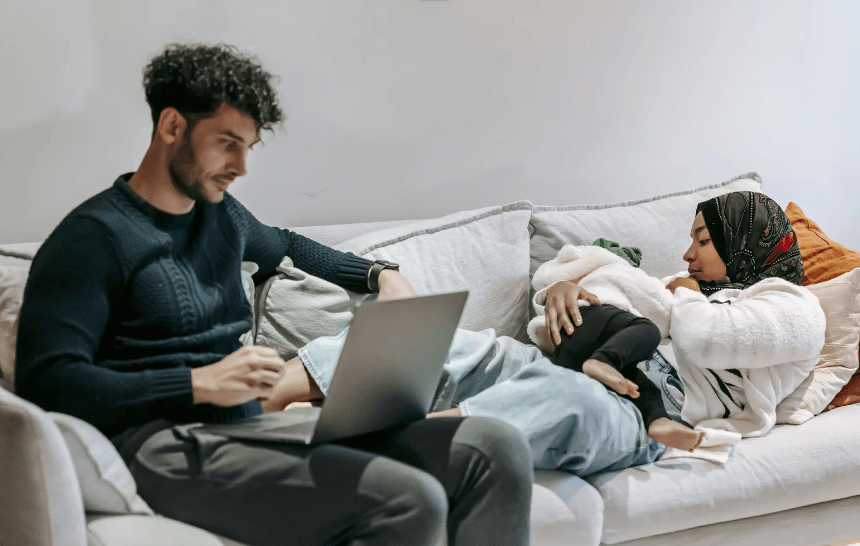 Mother breastfeeding on sofa while dad is accessing support on computer
